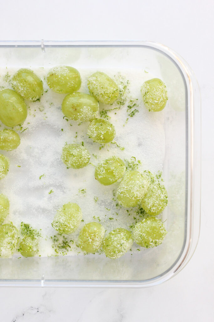 top down image showing a rectangle clear container filled with sugar and grapes