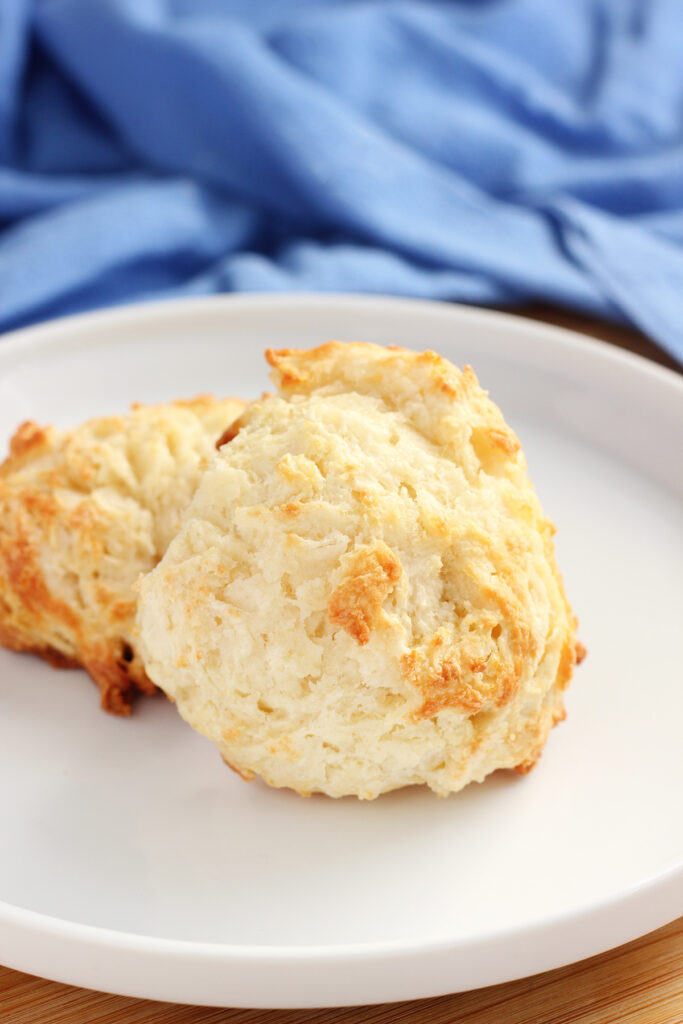 close up image of two biscuits on a white plate with a blue napkin off in the background. 