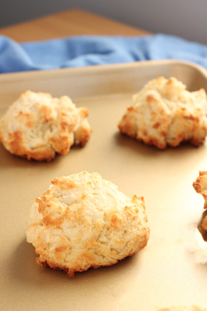 close up of biscuits sitting on a golden baking tray with a blue napkin off in the background
