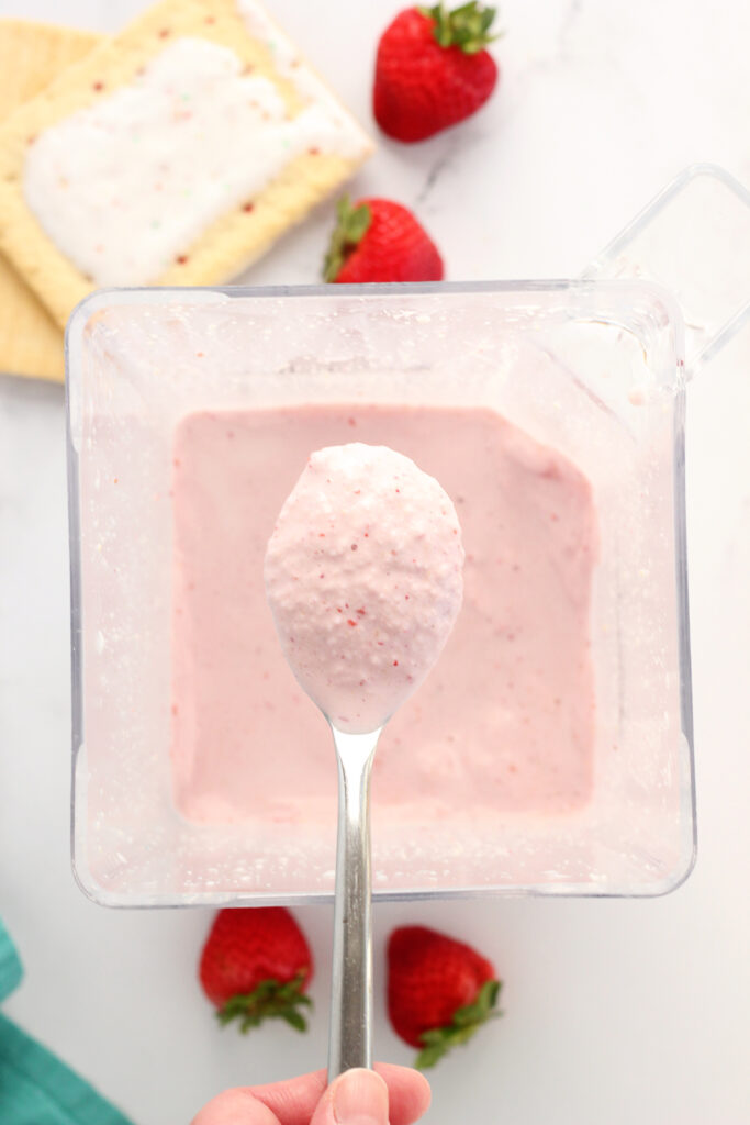 top down shot showing a spoon that is filled with a pink milkshake. The spoon is hovering over an open blender with more of the milkshake