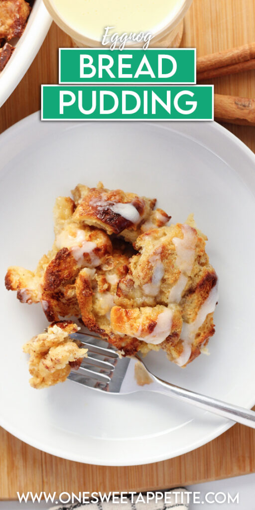 top down image showing a small white round plate with a serving of bread pudding on top. There is a drizzle of frosting and a bite on a fork. The plate is sitting on a wooden cutting board with a mug of eggnog and cinnamon sticks with a checkered white and black napkin. Text overlay reads eggnog bread pudding