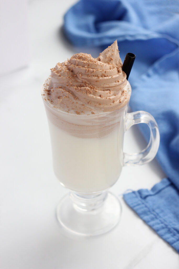 close up image showing a glass mug filled with chocolate whipped topping and chocolate shavings on a white table with a blue napkin