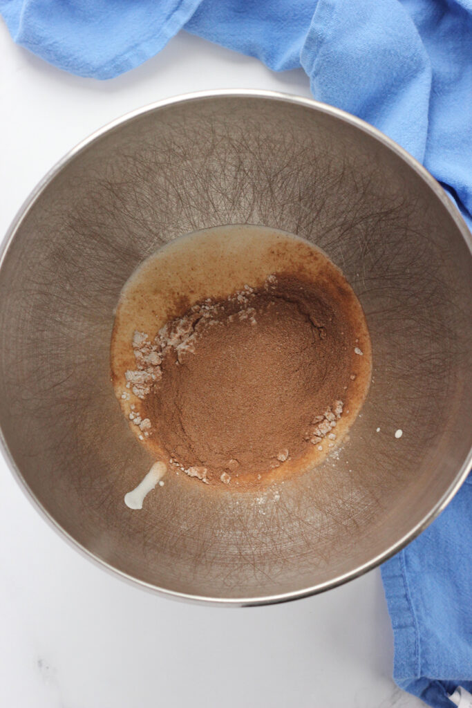 top down image showing the inside of a metal bowl with cream and cocoa mix inside on a white table top with a blue napkin