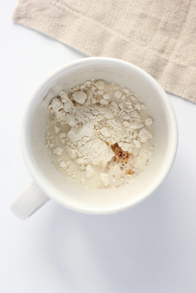 top down image showing a white mug filled with pancake mix, milk, vanilla, and oil