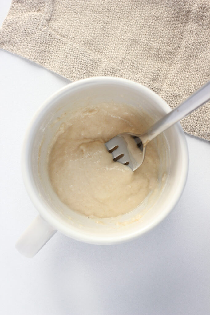 top down image showing a white mug filled with pancake mix that has been stirred with a fork