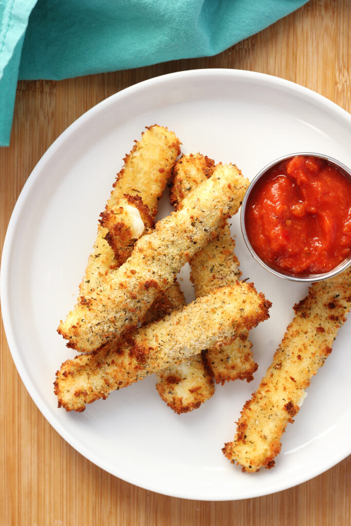 top down image showing a round white plate topped with crispy cheese sticks and a small round dish filled with marinara sauce