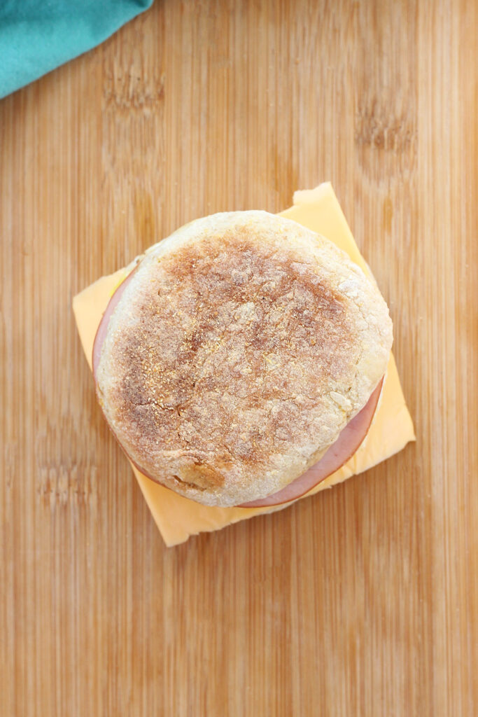 top down image showing an english muffin breakfast sandwich sitting on a wooden cutting board