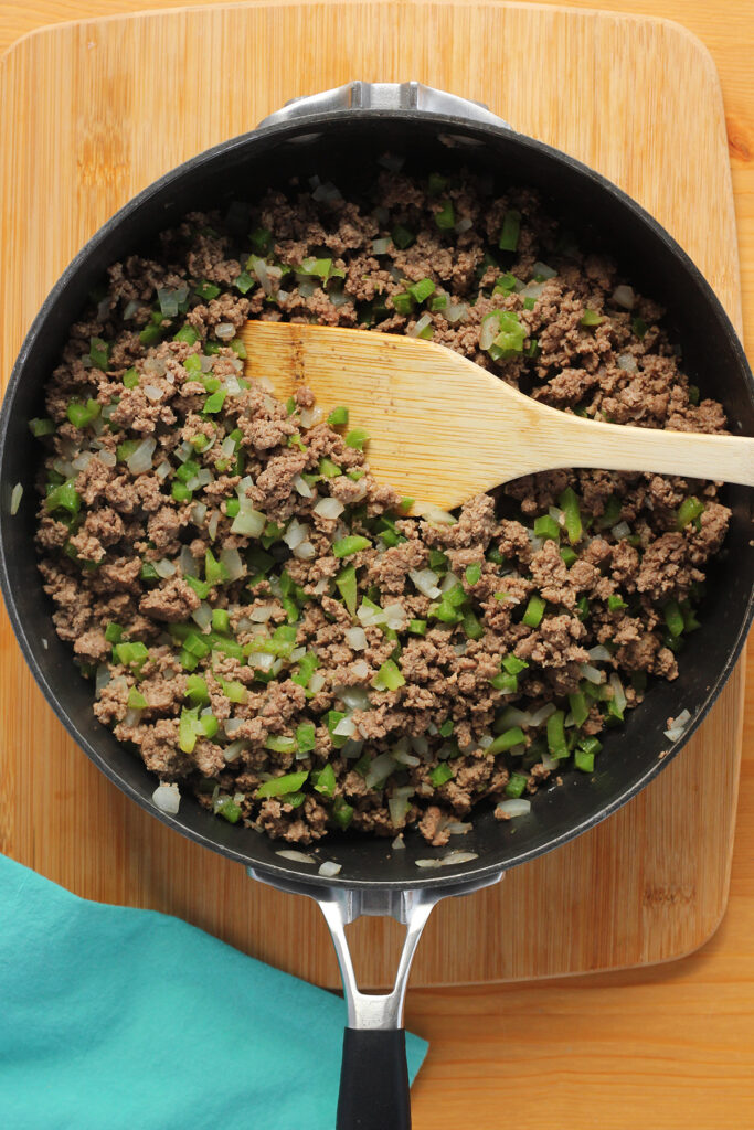 top down image showing cooked ground beef, onion, and bell pepper with a wooden spoon on a wooden table top