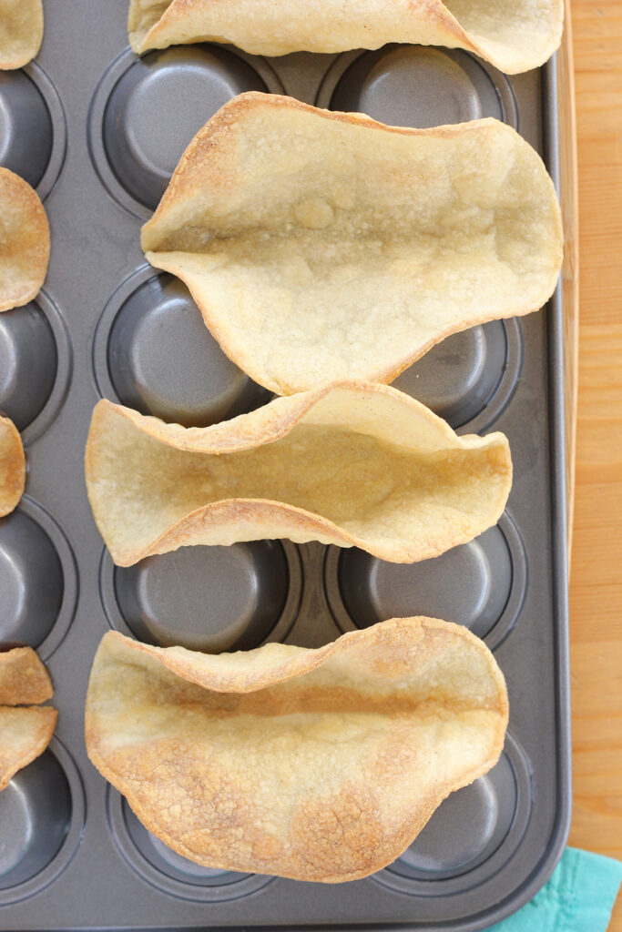 top down image showing a close up of baked tortillas shaped like tacos in an upside down cupcake tin