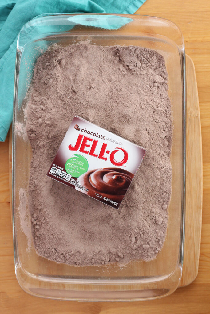 top down image showing dry cake mix in a 9x13 pan with a box of Jello chocolate pudding in the center