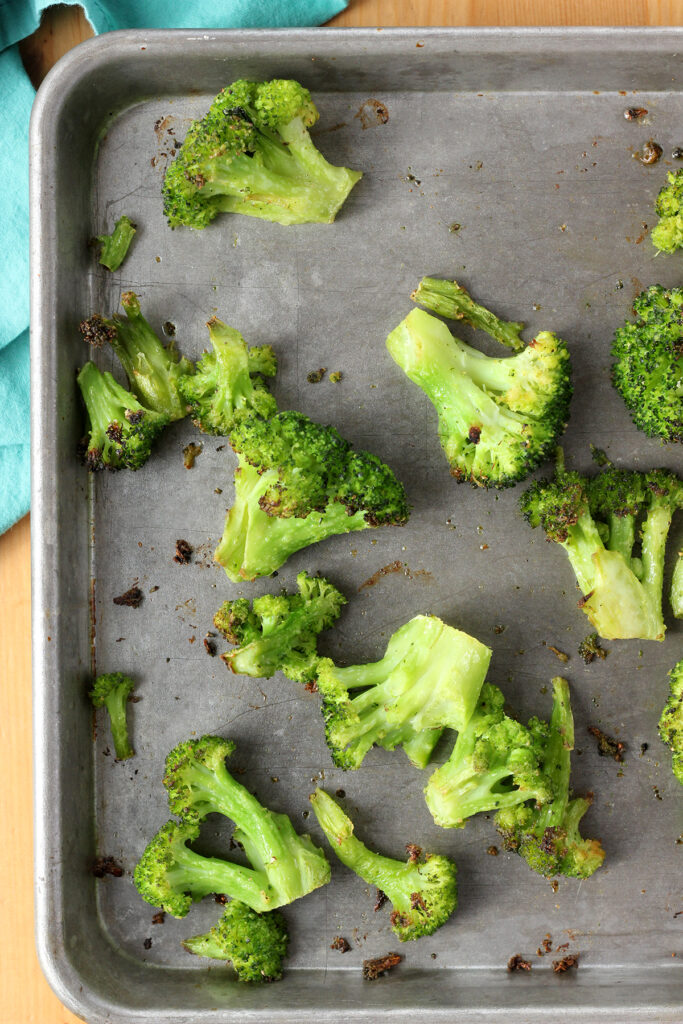 top down image showing a silver baking sheet covered in cooked broccoli 