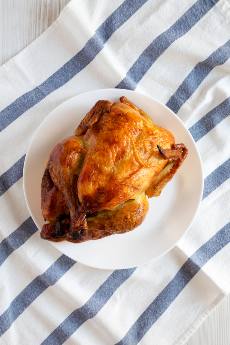 Rotisserie Chicken sitting ona white round plate with a blue and white stripe napkin