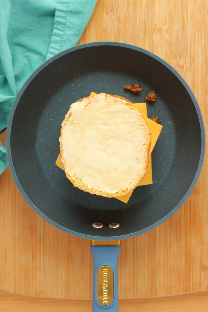 top down shot showing a blue skillet with an upside down bun topped with sloppy joe mix sitting on a wooden table top with a teal napkin off to the side. 