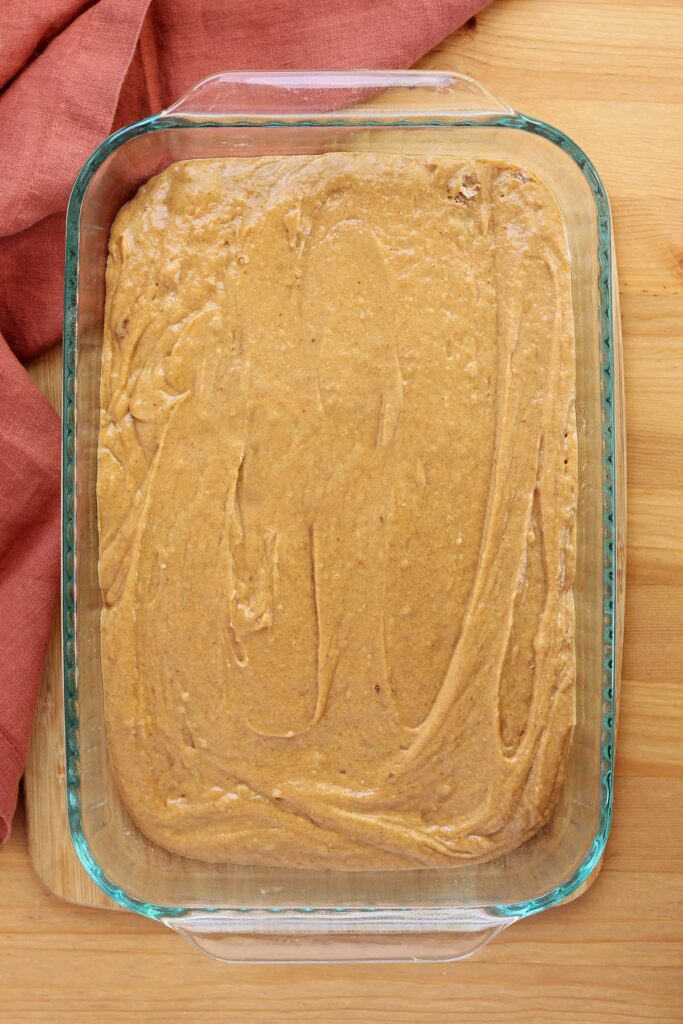 top dwon image showing a glass 9x13 pan sitting on a wooden table top with a pumpkin batter spread inside. There is a rust colored napkin off to the side.