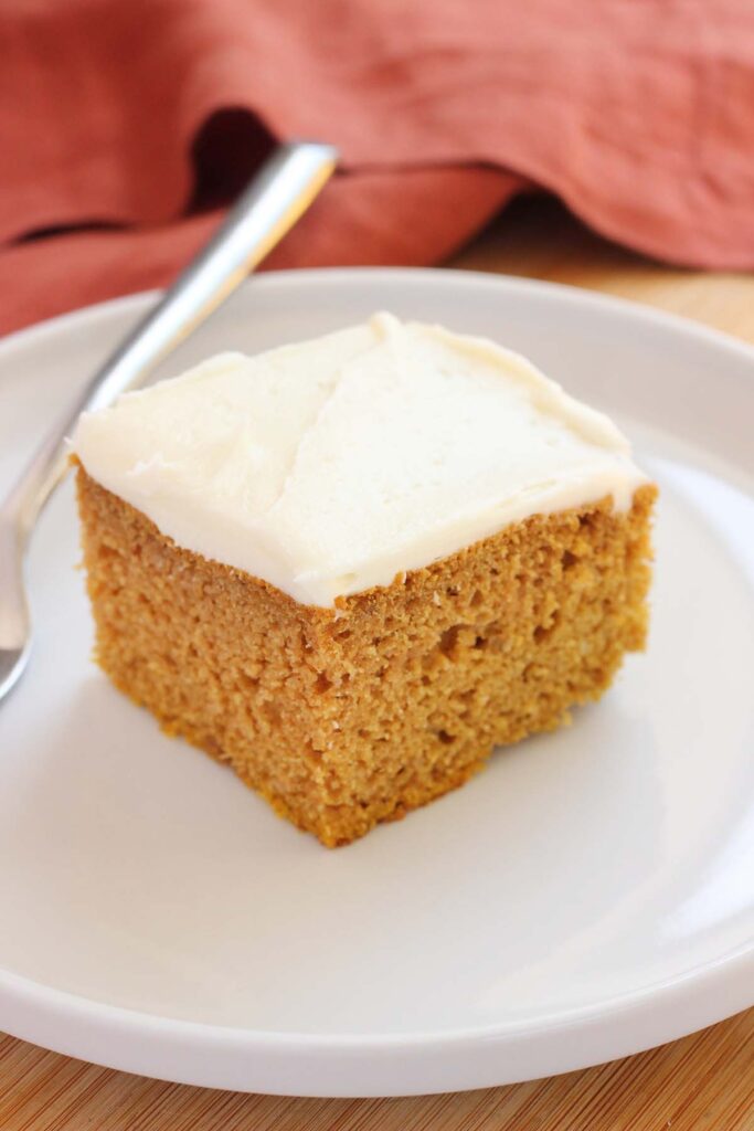 close up image of a piece of cake sitting on a white round plate. The cake is topped with a white frosting and a rust red napkin is off to the side