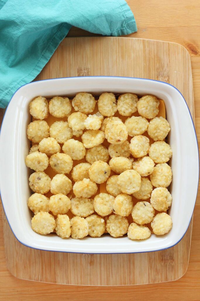 top down image showing a white baking dish filled with tater tots sitting on a wooden table with a teal napkin