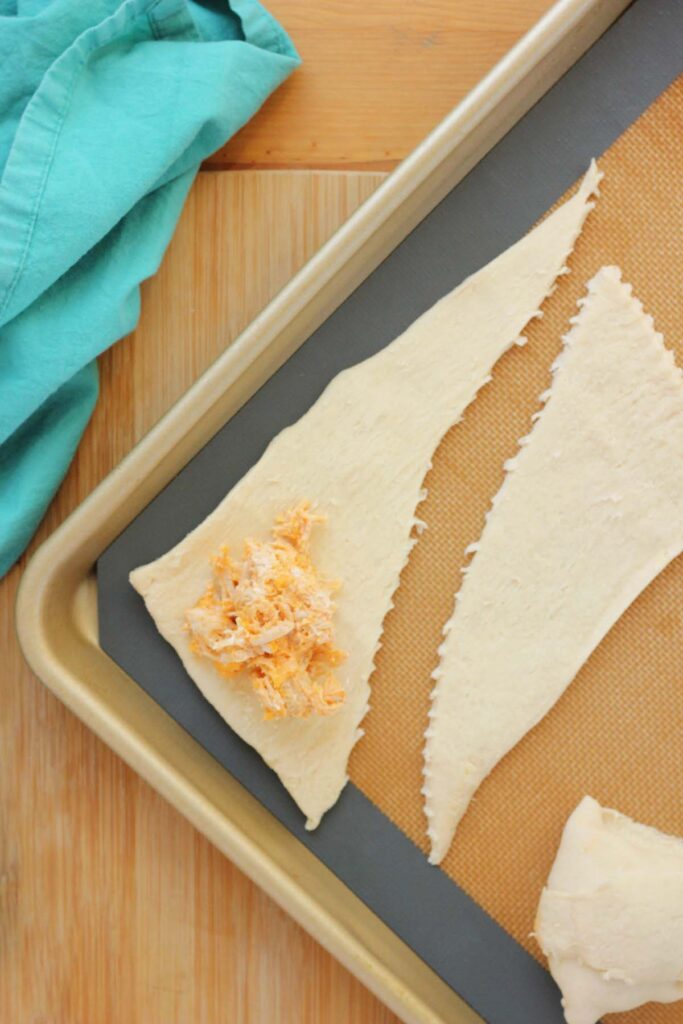 top down image showing a silicone mat lined tray with a triangle of dough with a spoonful of chicken mixture on top