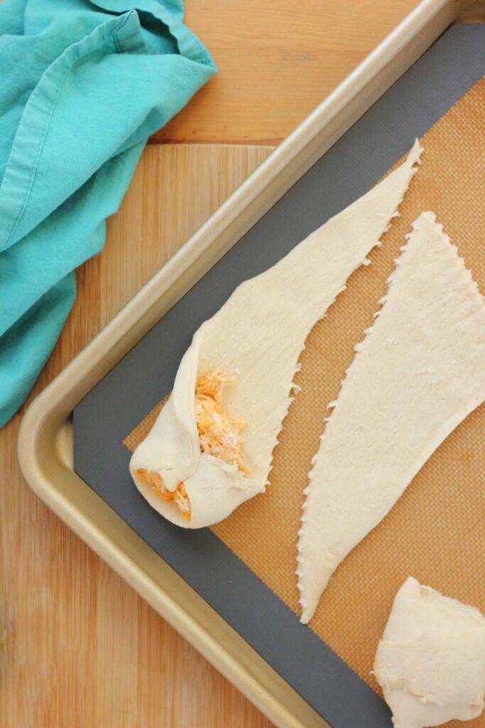 top down image showing a silicone mat lined tray with a triangle of dough with a spoonful of chicken mixture on top being wrapped