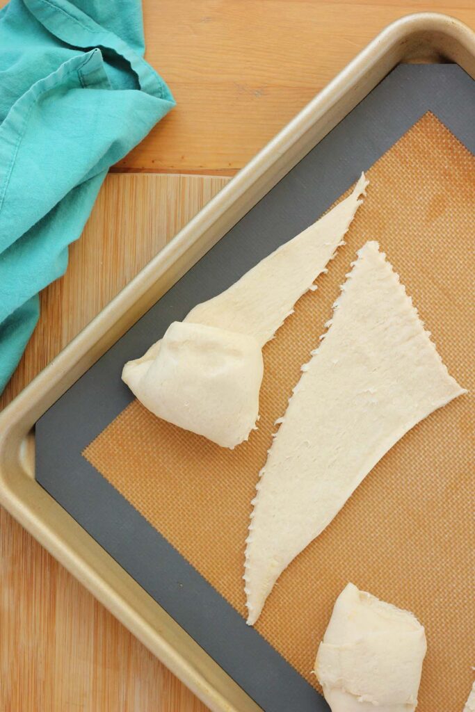 top down image showing a silicone mat lined tray with a triangle of dough with a spoonful of chicken mixture on top being wrapped