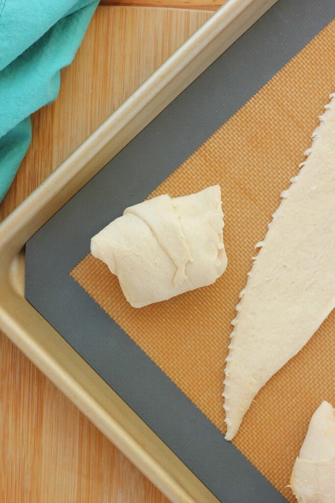 top down image showing a silicone mat lined tray with a triangle of dough with a spoonful of chicken mixture on top wrapped into a bundle