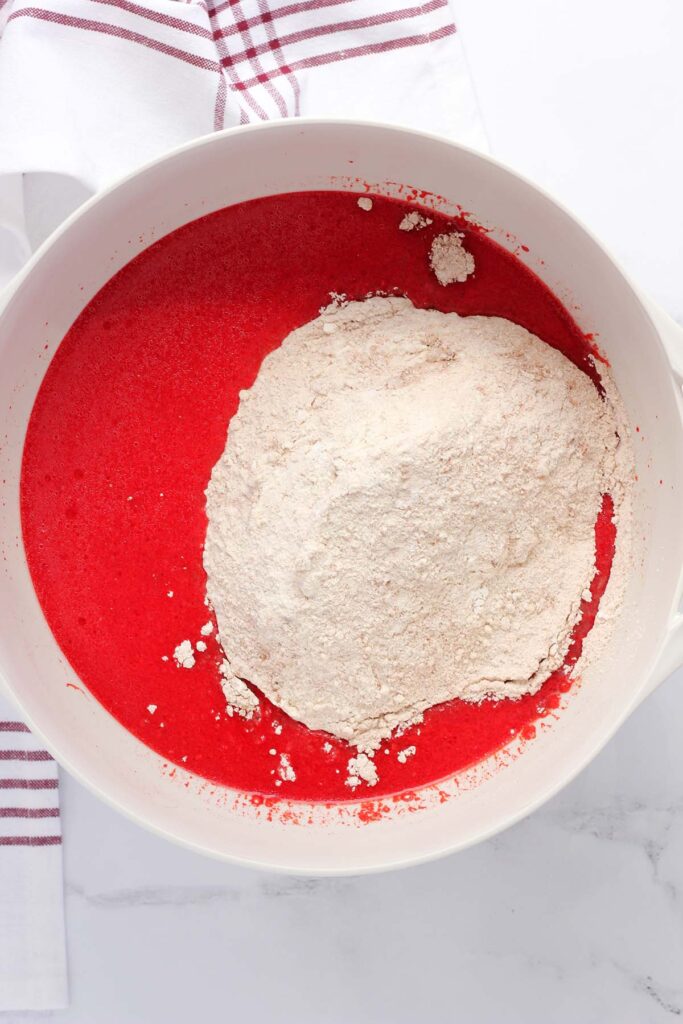 Top down image showing a white mixing bowl with red velvet batter and flour