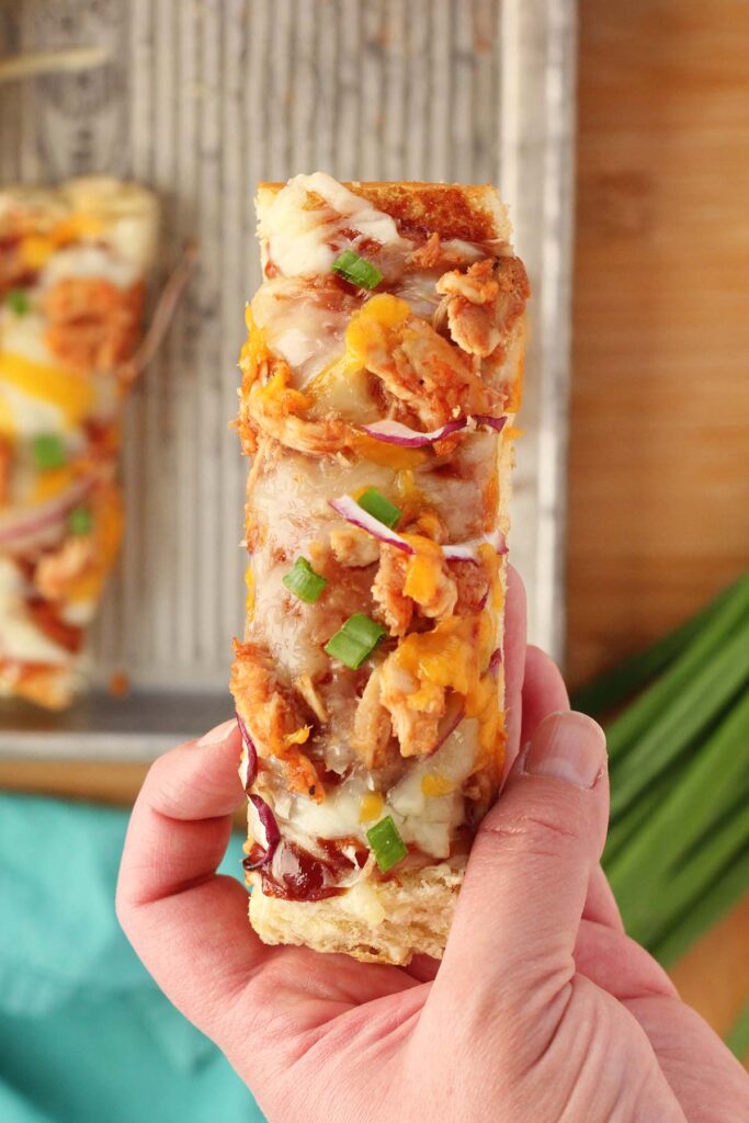 hand holding a thin slice piece of bread pizza with chicken cheese and onions