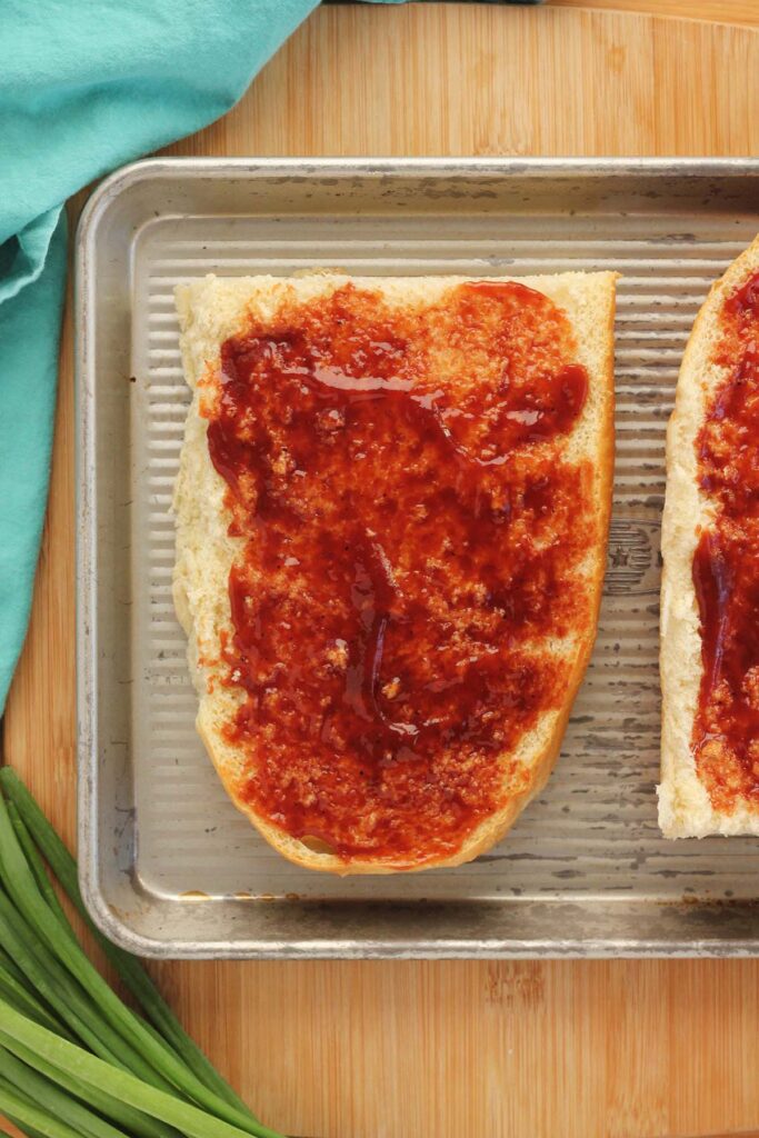 Top down image showing 1/2 a loaf of french bread sliced in half with bbq sauce spread across 