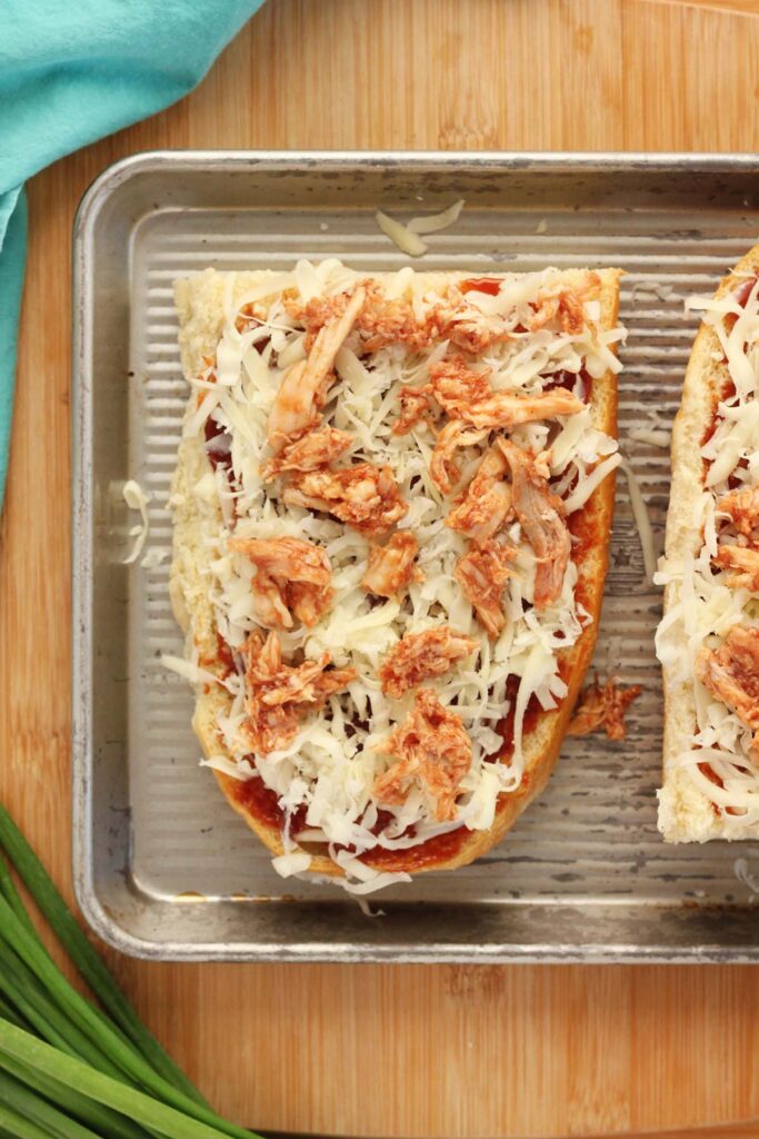 Top down image showing 1/2 a loaf of french bread sliced in half with bbq sauce spread across topped with cheese and chicken