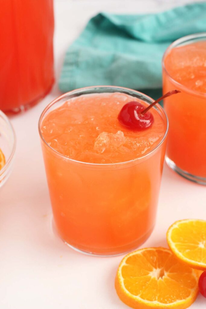 close up of a glass of redish orange punch with a cherry on top