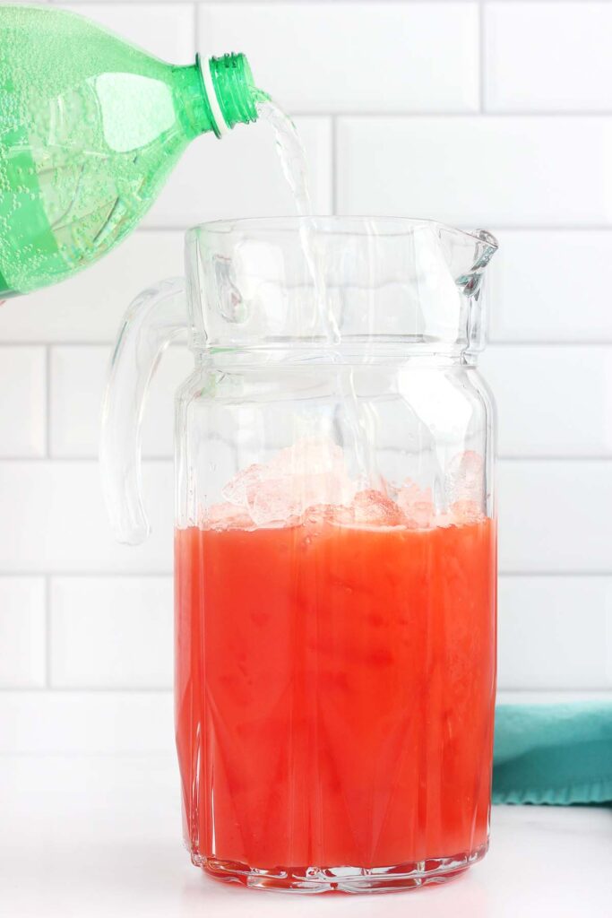 sprite being poured into a glass pitcher with red liquid inside