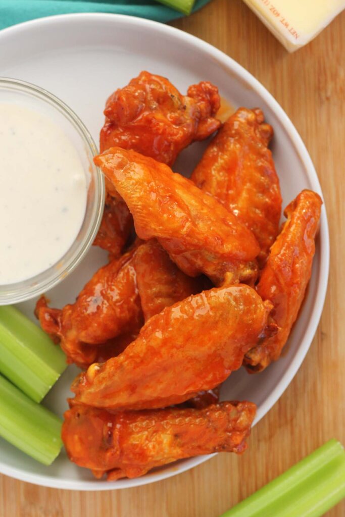 close up image showing a plate covered in hot wings with a bowl of ranch dressing and celery sticks in the background