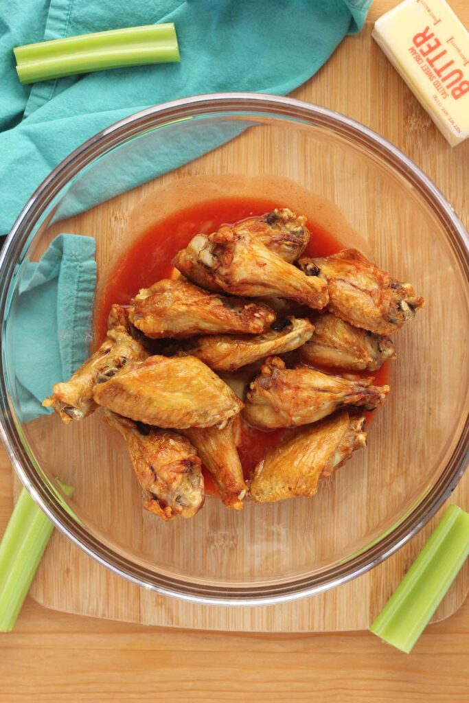 Top down image showing a glass bowl with sauce and cooked wings