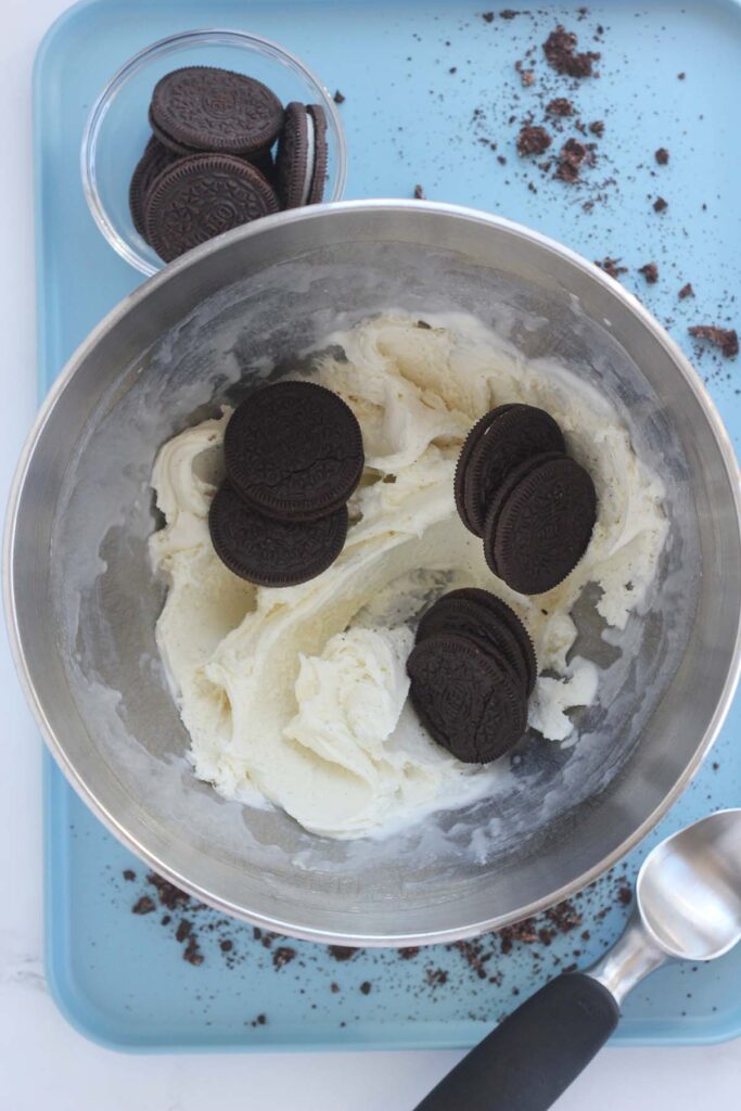 top down image showing a metal mixing bowl with vanilla ice cream that has been mixed with full chocolate sandwich cookies on top