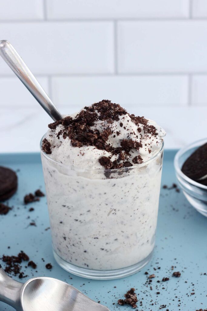 close up image showing a short glass filled with a speckled milkshake that is topped with cookie crumbs and a spoon.