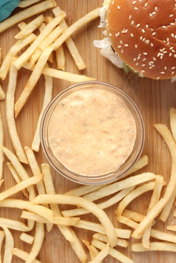 Top down shot showing a small glass bowl with a sauce with fries and a burger around the side