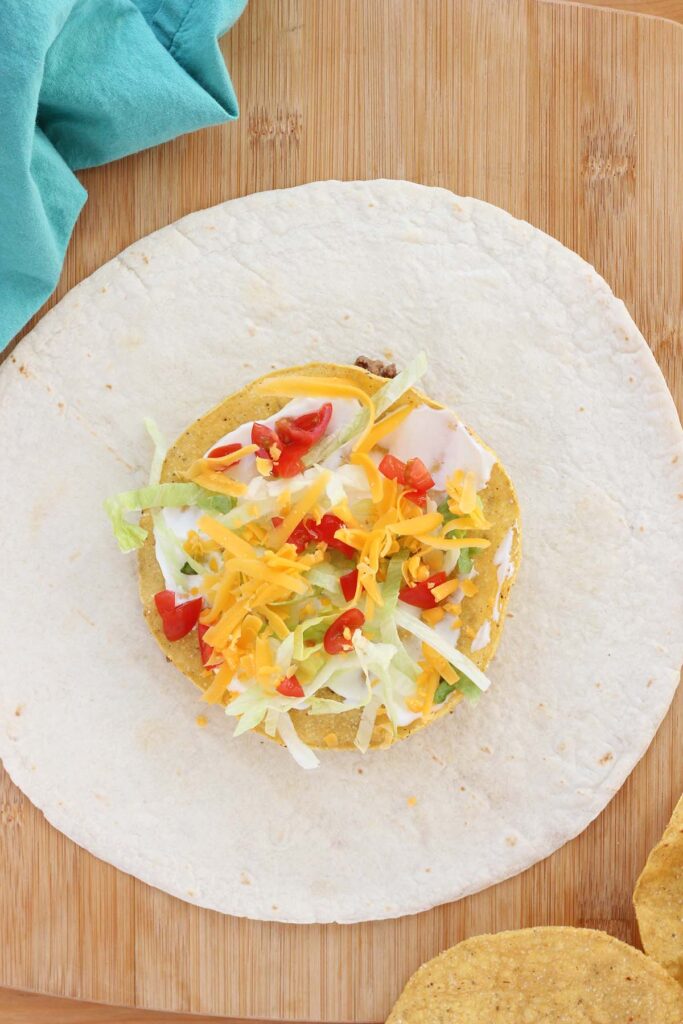 top down image showing a large tortilla topped with beef, tostada, sour cream, and lettuce with tomato and cheese
