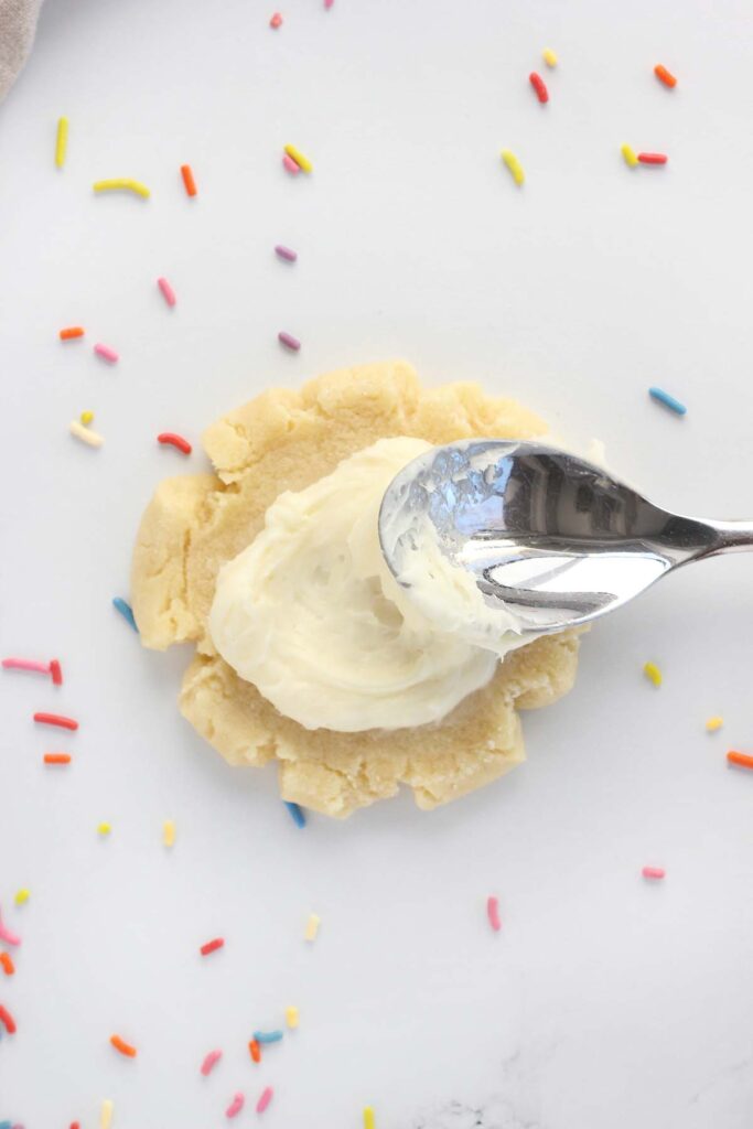 frosting being spread onto a smashed sugar cookie with sprinkles around