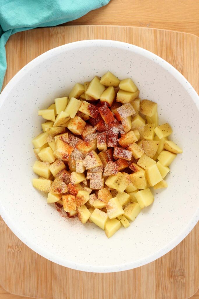 top down image showing a white mixing bowl filled with dried potato pieces with seasonings