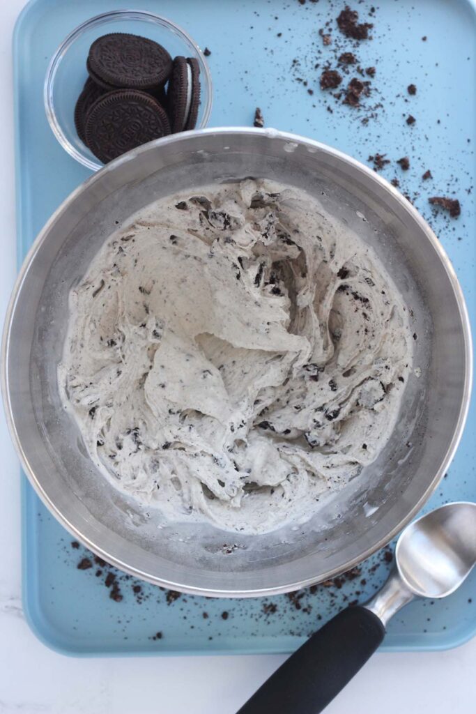 top down image showing a metal mixing bowl with vanilla ice cream that has been mixed with full chocolate sandwich cookies mixed in