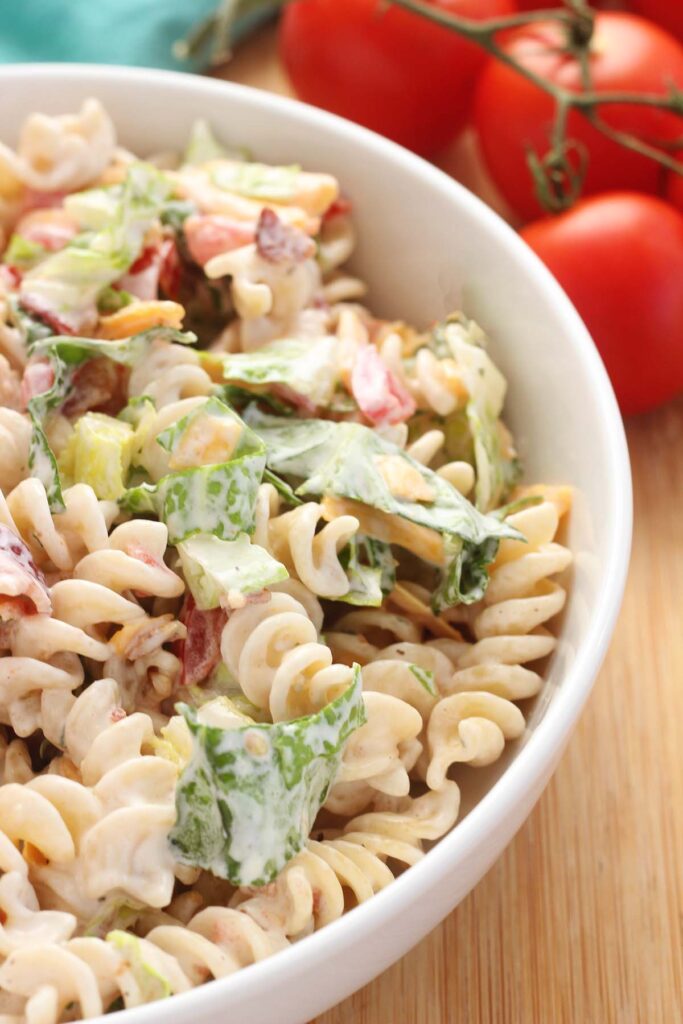 close up image showing a pasta dish with a creamy dressing with lettuce and bacon and tomato in a white bowl
