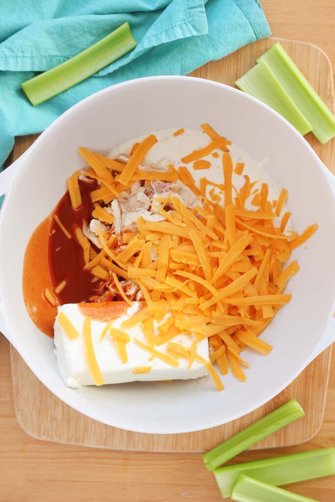 Top down image showing a white mixing bowl filled with cream cheese, buffalo sauce, shredded cheddar, and ranch dressing.