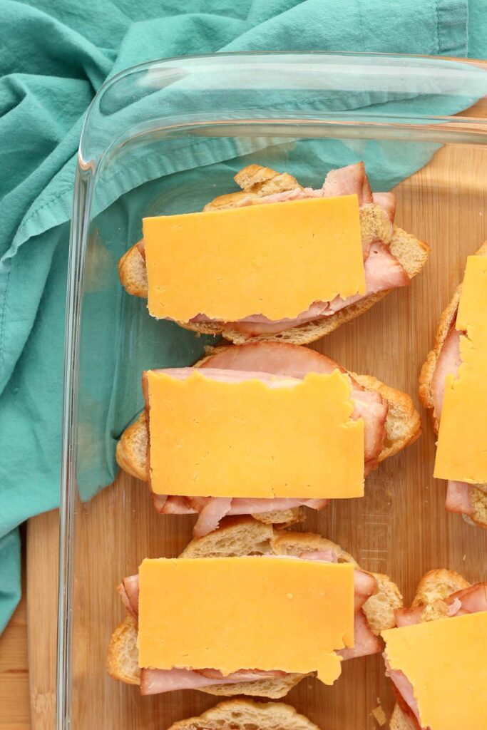 top down image showing a sliced open croissant layered with ham and cheese in a glass baking dish