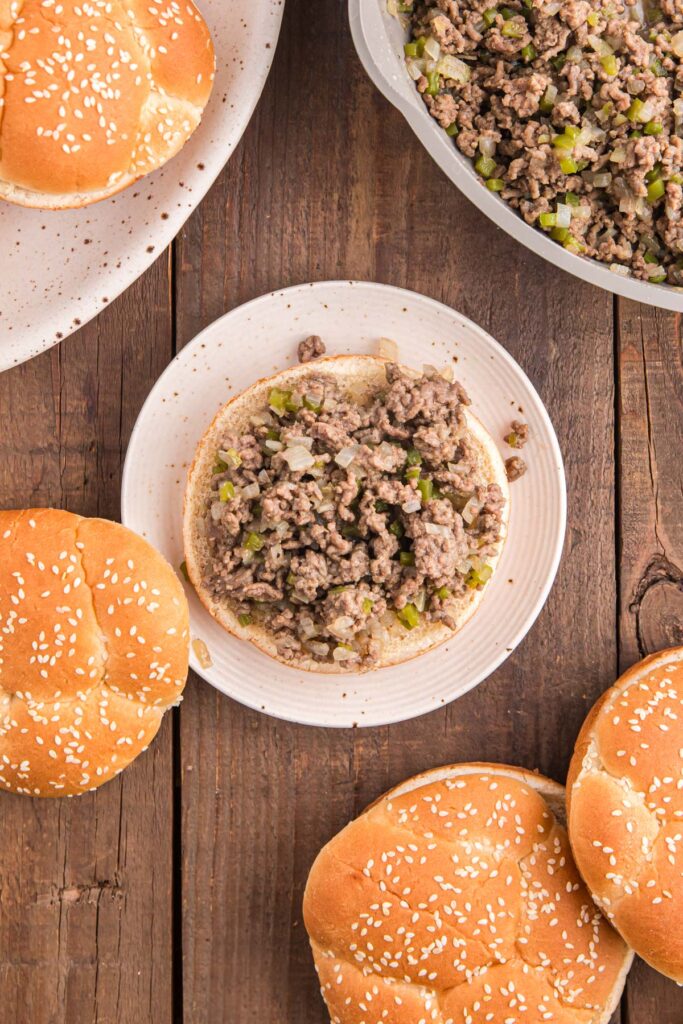 Top down image showing a bun on a white plate topped with a meat mixture