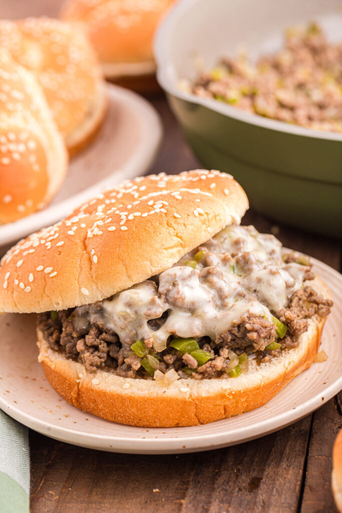 close up image showing a sloppy joe with peppers and melted cheese in a bun sitting on a white plate