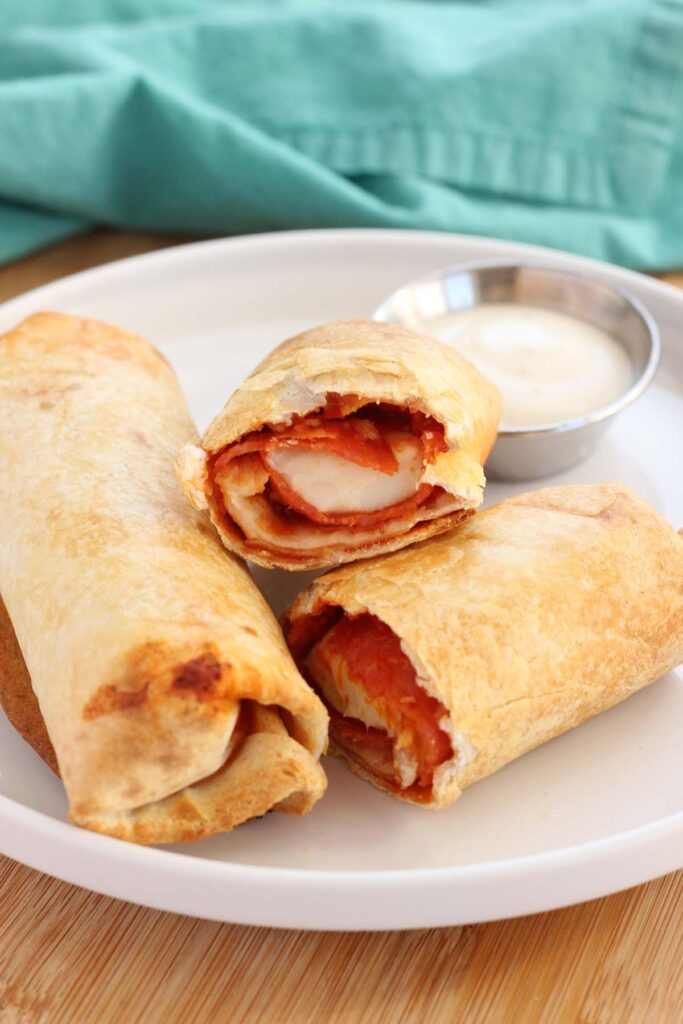 close up image showing burritos stuffed with cheese and pepperoni stuffed burritos stacked on a white plate