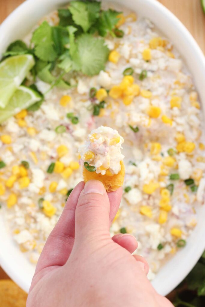 top down image showing a dip being scooped out onto a chip with corn and cilantro