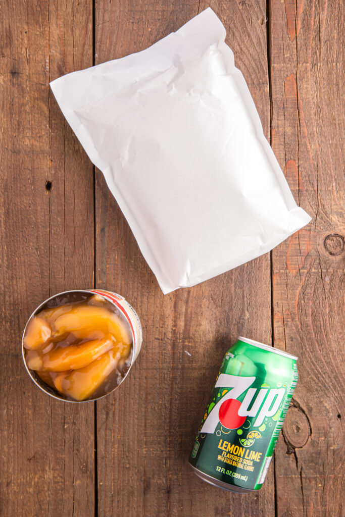 Top down image showing a cake mix inside abag, open can of peach pie filling, and a can of seven up