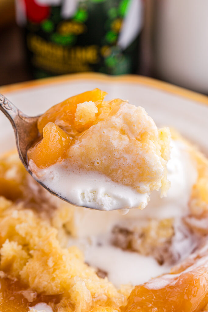 close up showing a spoon that has scooped a bite of cobbler with ice cream over a bowl with more cobbler