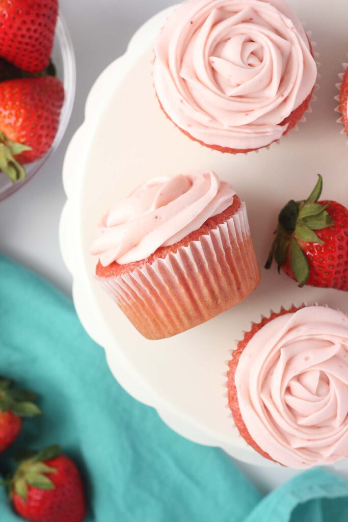 Top down image showing three cupcakes that are frosted with pink frosting to look like roses. 