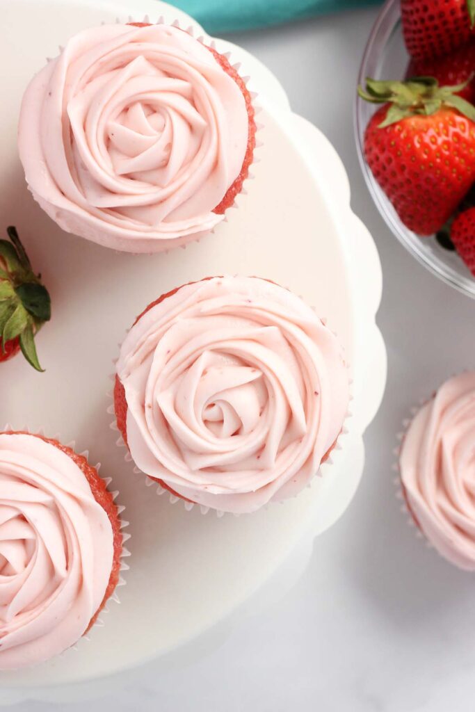 Top down image showing three cupcakes that are frosted with pink frosting to look like roses. 